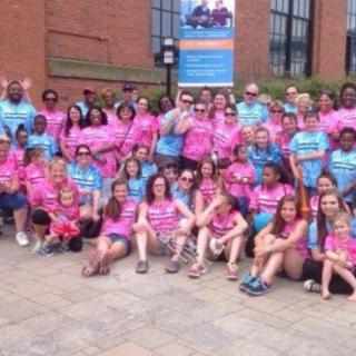 A large group of people wearing colorful event t-shirts pose for a photo in front of a brick building.