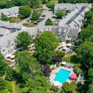 Aerial view of a hotel complex with a central swimming pool surrounded by lush gardens and trees.