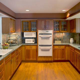 A modern kitchen with wooden cabinets, built-in oven and microwave, and hardwood flooring.
