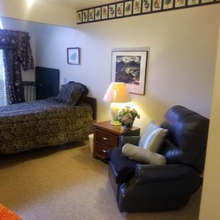 A cozy bedroom featuring a single bed, an armchair, and warm lighting.