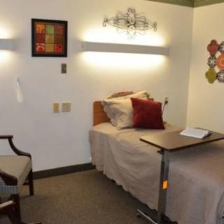 A cozy hospital room with a single bed, side chair, and warm lighting.