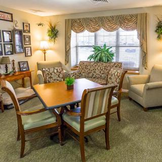 A cozy living room featuring a dining table with chairs, a patterned sofa, an armchair, and indoor plants near the window.