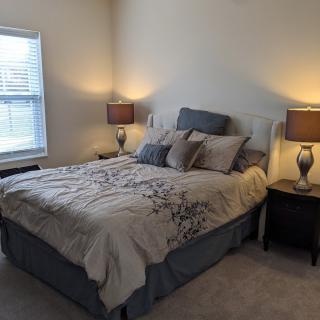 A cozy bedroom with a well-made bed, flanked by two nightstands and lamps, illuminated softly by natural light from a nearby window.