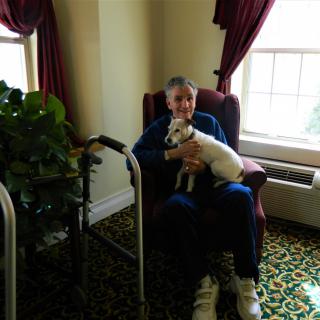 An elderly person sitting in a chair holding a small dog in a cozy room.