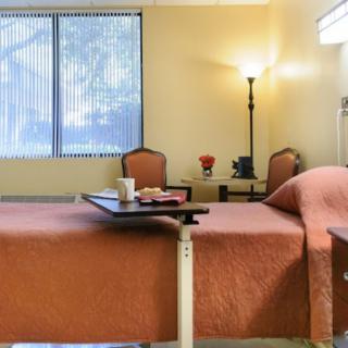 A cozy hospital room with a bed, tray table, and warm lighting.