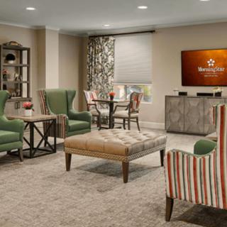 A cozy living room featuring comfortable armchairs, a central ottoman, and a TV area.