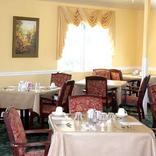 An elegantly set dining room with several tables and chairs, featuring a window and a painting on the wall.
