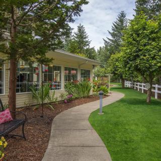 A scenic garden pathway lined with lush greenery and trees, bordered by a white fence.