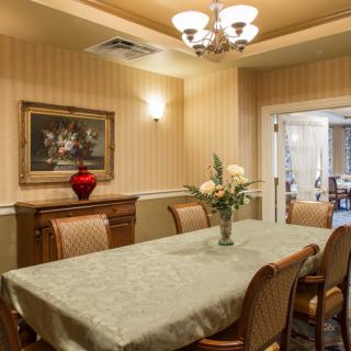 A warmly decorated dining room with a long table and upholstered chairs, adorned by a chandelier and a painting on the wall.