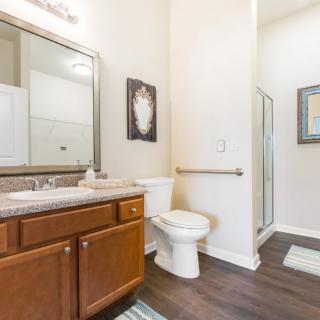 A modern bathroom featuring a wooden cabinet, toilet, sink with mirror, and a glass-enclosed shower.