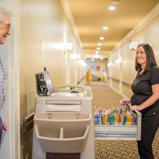 A janitor with a cleaning cart converses with a person in a hallway.