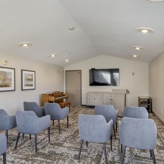 A modern meeting room with a conference setup, featuring several chairs facing a television on a carpeted floor.