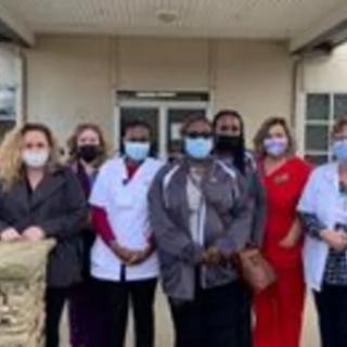 A group of people, including healthcare workers wearing masks, standing outside a building.