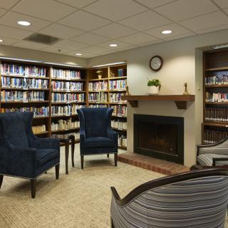 A cozy library reading area with bookshelves, a fireplace, and comfortable chairs.