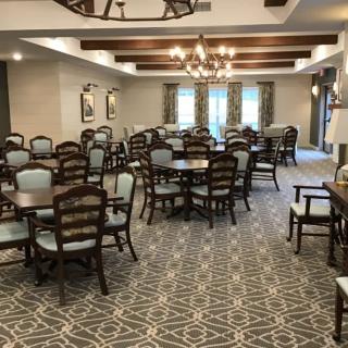 A spacious dining area with multiple tables and chairs, featuring chandeliers and decorative ceiling beams.