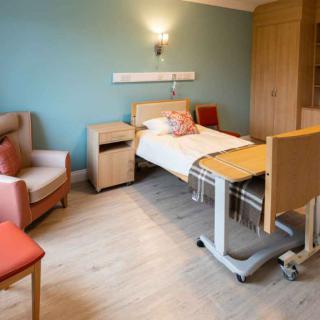 A well-furnished hospital room featuring a bed, side table, and chairs.