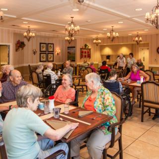 A group of seniors socializing and dining in a communal indoor setting.
