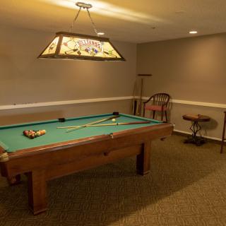 A cozy game room featuring a pool table with overhead lighting.