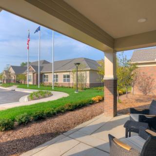 A sunny view from a covered patio looking towards a building with flags and landscaped surroundings.
