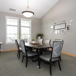 A modern dining room with a large table and elegant chairs, featuring ample natural light from two large windows.