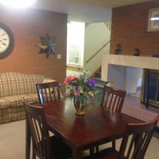 A cozy living and dining area featuring a wooden dining table adorned with flowers, surrounded by chairs, and a comfortable sofa in the background.