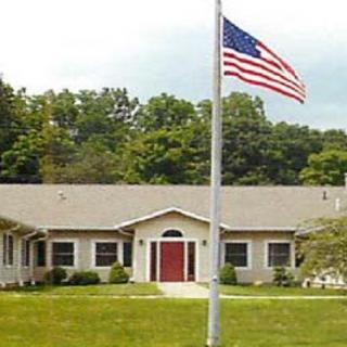 A building with an American flag in front and a lawn surrounded by trees.