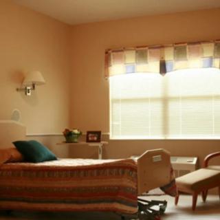 A hospital room with a bed, chair, and window.