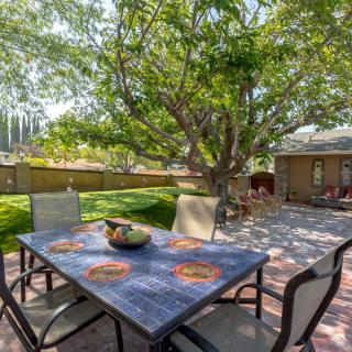 A sunny backyard patio with a table and chairs under a large tree.