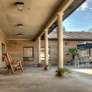 A serene porch with a rocking chair, columns, and greenery, perfect for unwinding in the sunlight.