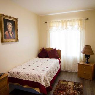 A cozy bedroom with a single bed, decorated with a portrait and warm lighting.