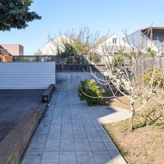 A sunny garden with a paved pathway, trees, and a wooden deck.