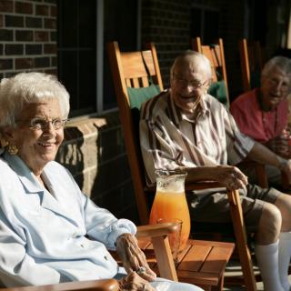 A group of elderly people enjoying a sunny day sitting on rocking chairs on the porch.