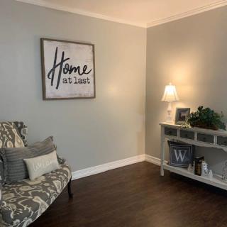 A cozy living room corner featuring a patterned chair, side table with decorations, and wall art saying 'Home'.
