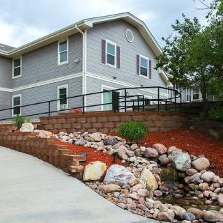 A modern two-story house with a landscaped garden featuring a retaining wall and rocks alongside a driveway.