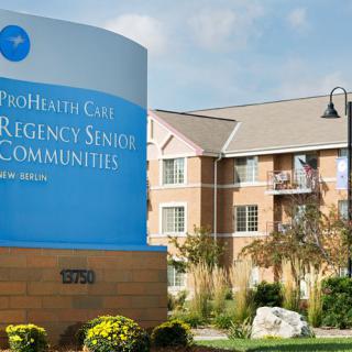 Entrance to the ProHealth Care Regency Senior Communities building with landscaped surroundings.