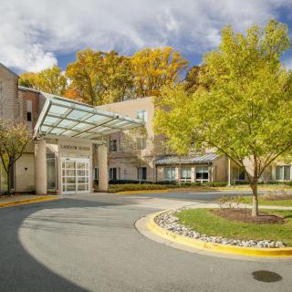 A building entrance with a glass canopy, surrounded by trees and landscaped grounds in autumn.