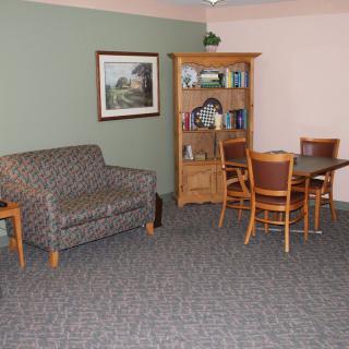 A cozy living room with a patterned sofa, wooden bookshelf, and a dining table with chairs.