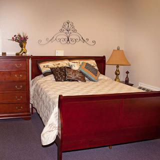 A cozy bedroom with a wooden bed and dresser, adorned with decorative pillows and a stylish lamp.