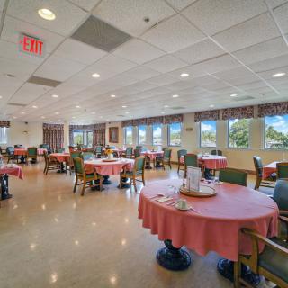A spacious dining room with neatly arranged tables and chairs, featuring large windows and bright lighting.