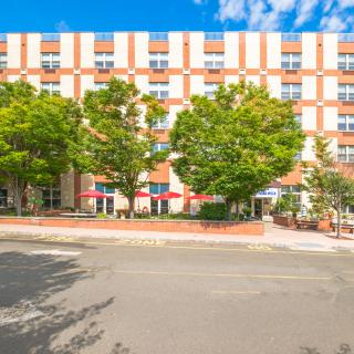 A sunny day view of a hotel building with trees lining the street.