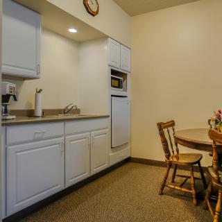 A compact kitchen area with white cabinets, a dining table with chairs, and a wall clock.