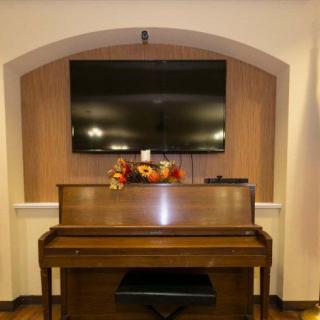 A room featuring a piano with autumn decorations, beneath a wall-mounted television within an arched alcove.