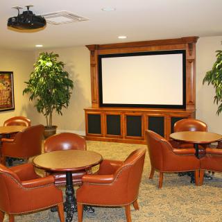 A conference room with tables, chairs, a projector screen, and decorative plants.