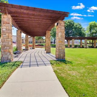 A scenic outdoor walkway with a wooden pergola and stone pillars under a clear blue sky.