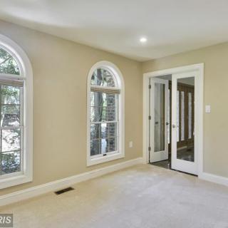 A spacious room with arched windows, carpet flooring, and glass doors allowing for natural light.