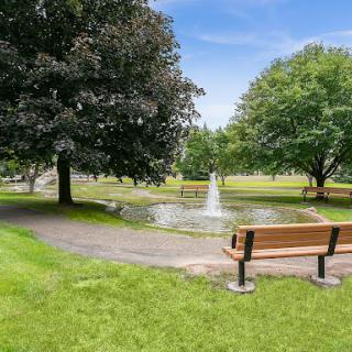 A serene park setting featuring a small fountain surrounded by lush greenery and benches.