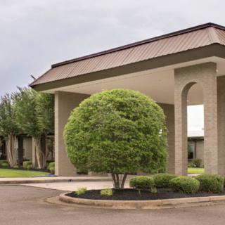 A modern building with a circular driveway and a neatly trimmed bush in the foreground.