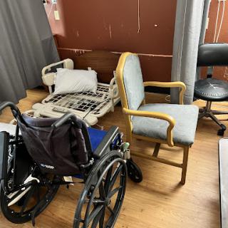 A room with a wheelchair, a chair, and a disassembled hospital bed.