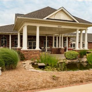 A charming house with a porch supported by white columns, surrounded by a well-maintained garden and a small pond.