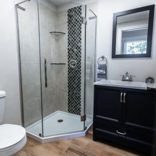 A modern bathroom featuring a glass-enclosed shower, a dark vanity with a sink and mirror, and tile flooring.